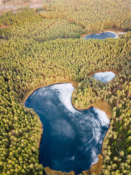 Luftaufnahme eines teilweise zugefrorenen Sees, umgeben von schönen grünen Farben der Felder und Wälder - Foto, Bild