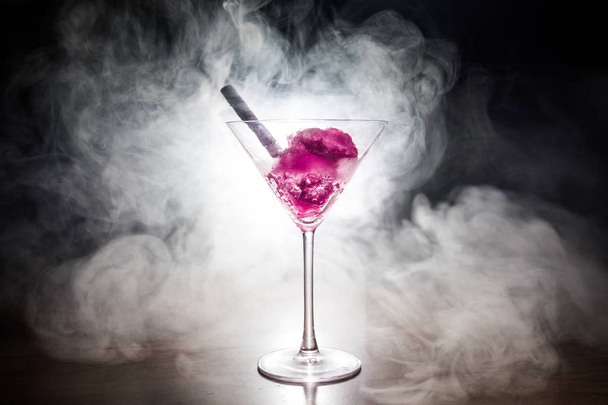 Martini-Glas gefüllt mit buntem Fruchteis auf dunklem Hintergrund mit getöntem Licht und Nebel. Selektiver Fokus - Foto, Bild