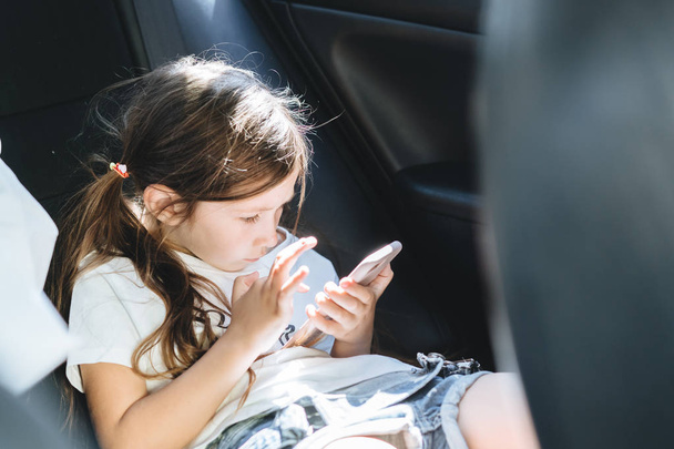 mała dziewczynka w samochodzie, patrząc na smartphone - Zdjęcie, obraz