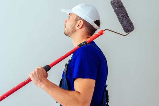 Guy in blue uniform hold paint roller on white wall - Photo, Image
