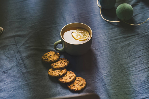 Tea with Lemon and Cookies with Chocolate Laying on Mattress - Blurred Turquoise Cover in Background with Pillow, Vintage Look Edit - Фото, зображення