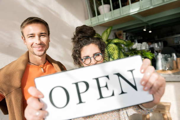 Woman wearing glasses holding open sign opening cafe with husband - Photo, Image