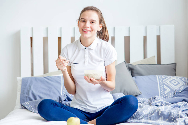 Smiling healthy girl eating corn flakes cereal and having breakfast - Zdjęcie, obraz