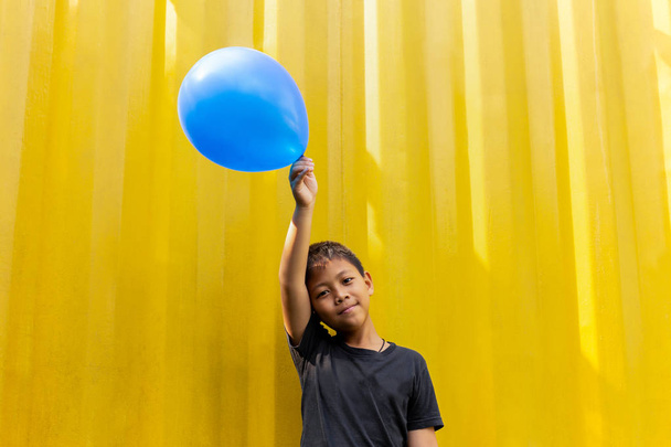 Chłopiec trzyma niebieskie balony, stojąc na żółtym tle - Zdjęcie, obraz