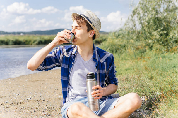 hiker is taking a break and drinking tea or coffee from a thermos - Foto, Bild