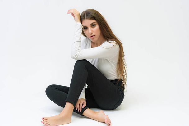 Studio portrait of a smiling happy beautiful brunette girl on a white background talking and sitting on the floor. She is right in front of the camera in various poses. - Фото, зображення