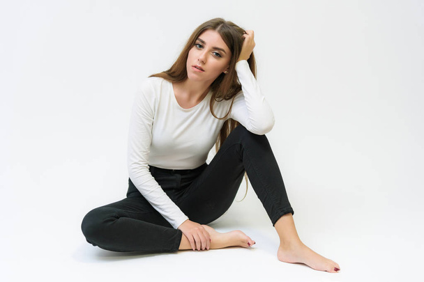 Studio portrait of a smiling happy beautiful brunette girl on a white background talking and sitting on the floor. She is right in front of the camera in various poses. - Foto, immagini
