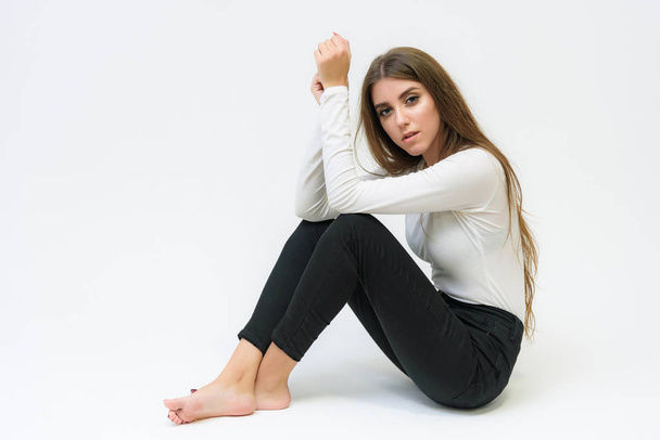 Studio portrait of a smiling happy beautiful brunette girl on a white background talking and sitting on the floor. She is right in front of the camera in various poses. - Foto, Imagem