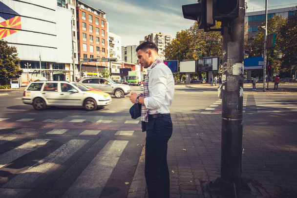 Jovem empresário está na cidade grande urbana, ele está de pé e esperando no pedestre, tentando atravessá-lo
 - Foto, Imagem