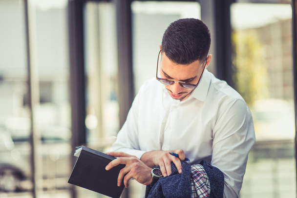 Σύγχρονο επιχειρηματία κρατώντας σημειώσεις ενώ ψάχνει σε ρολόι του ενώ στέκεται έξω - Φωτογραφία, εικόνα