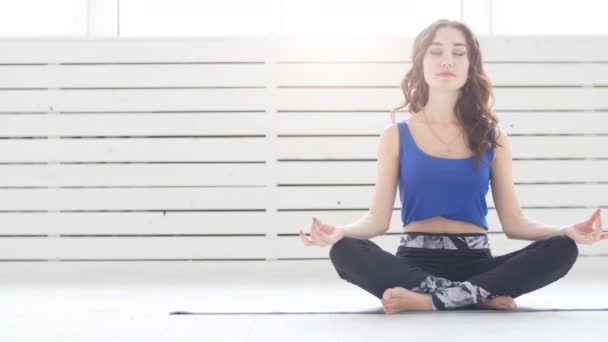 Mujer joven y deportiva practicando yoga, sentada en medio ejercicio de loto, pose Siddhasana, interior, fondo interior del hogar
 - Metraje, vídeo