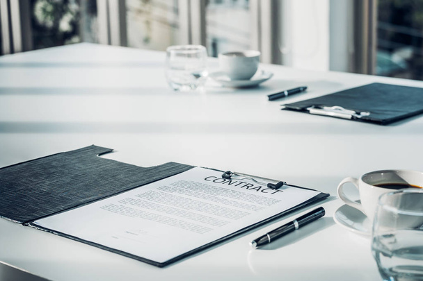 Close up business contract paper on meeting room table with pen and coffee cup in sun light shadow with green plant at office,business agreement concept - Photo, image