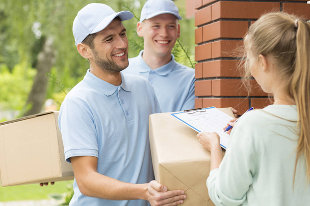 Two smiling couriers in blue uniforms and young women filling up delivery documents - Foto, Imagen
