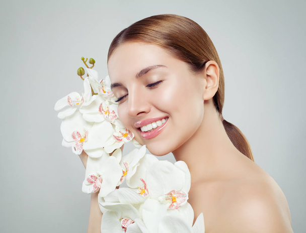 Mulher spa bonita com pele saudável, sorriso bonito e flor de orquídea no fundo branco, retrato sloseup
 - Foto, Imagem