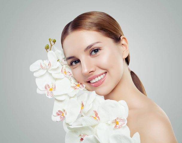 Mladá usměvavá žena zdravé kůže a bílé květy orchidejí. Kosmetika, spa krása, kosmetika a obličeje ošetřovatelský koncept  - Fotografie, Obrázek