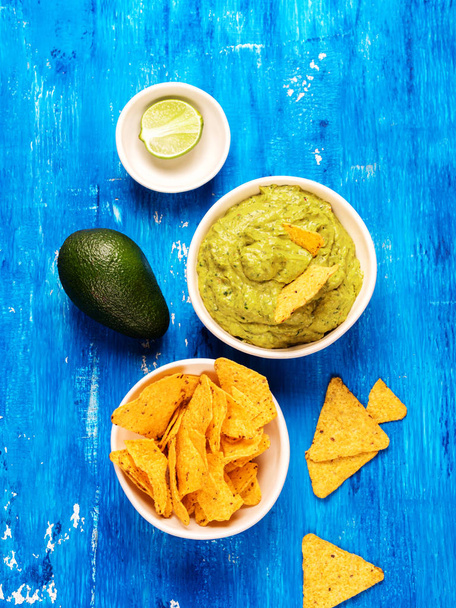 Fresh guacamole sauce in bowl and Mexican corn chips nachos with fresh avocado and lime on blue background - Zdjęcie, obraz