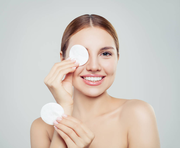 Cheerful woman removing face makeup with a cotton pad on white background - Foto, afbeelding