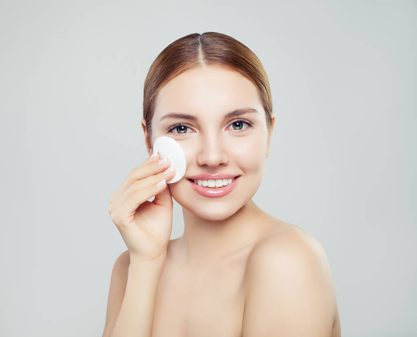 Attractive woman cleaning her face with a cotton pad and smiling on gray backgroun - Photo, Image