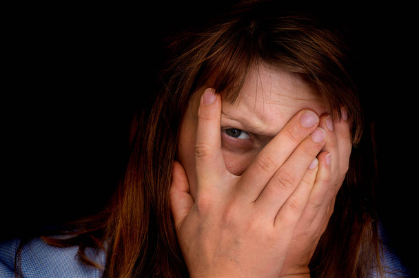 junge Frau bedeckt ihr Gesicht mit den Händen und blickt mit einem Auge in die Kamera - isoliert auf schwarzem Hintergrund - Foto, Bild