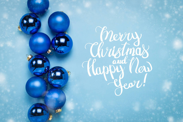 Blue Christmas tree toys, balls on a blue background with falling snow. Added text Merry Christmas and Happy New Year. Flat lay, top view. - Photo, image