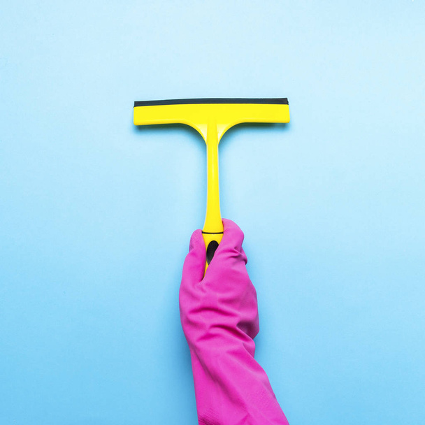 Mão feminina em luvas rosa segurando um raspador para limpar janelas em um fundo azul. conceito de serviço de limpeza. Flat lay, vista superior
. - Foto, Imagem
