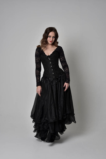 full length portrait of brunette girl wearing long black lace gown wit corset. standing pose, isolated on grey studio background. - Fotoğraf, Görsel