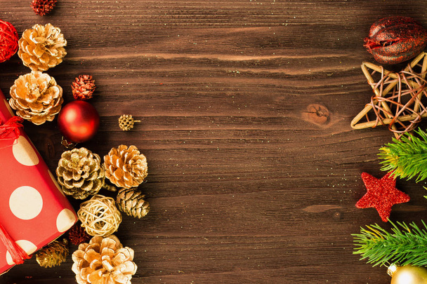Natale e Capodanno decorazione, palle, coni di abete, rami e stelle di legno con regalo avvolto in carta rossa con cerchi d'oro su sfondo legno. Piatto. Vista dall'alto. Copia spazio per testo
. - Foto, immagini