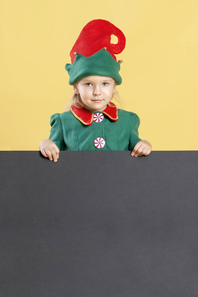 Κοριτσάκι σε Χριστουγεννιάτικο ξωτικό κοστούμι στέκεται με χώρο για κείμενο σε κίτρινο φόντο - Φωτογραφία, εικόνα