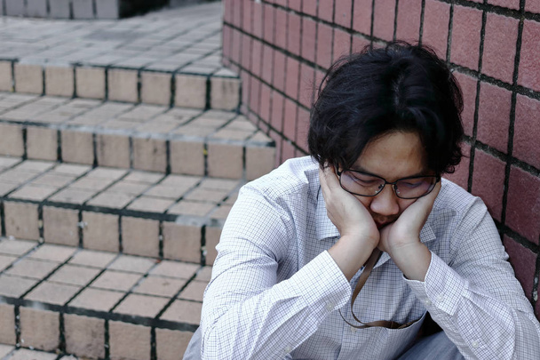 Απογοητευμένοι εξαντληθεί Ασίας επιχείρηση άνθρωπος σε κατάθλιψη με τα χέρια στο πρόσωπο κάθεται σε εξωτερικούς χώρους. - Φωτογραφία, εικόνα