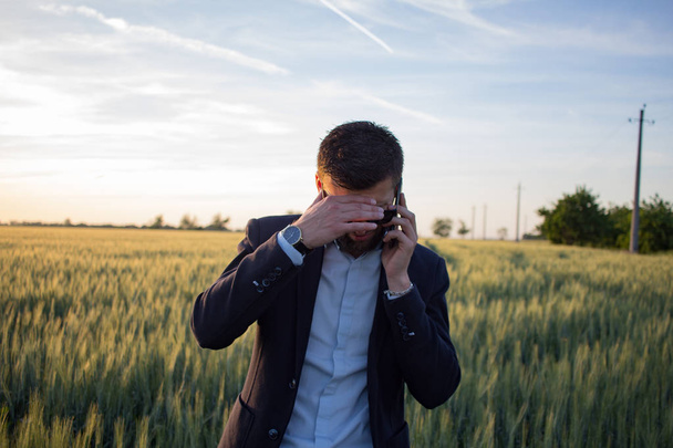 Young man in black suit speacking on phone in wheat field, during beautiful sunset - Foto, Bild