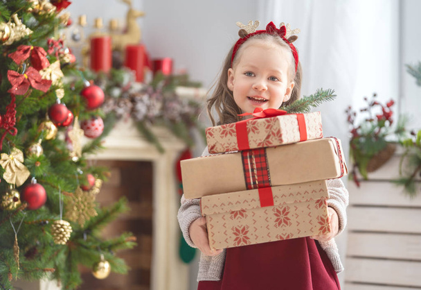 Merry Christmas and Happy Holiday! Cute little child girl with present gift boxes near tree at home. - Foto, afbeelding