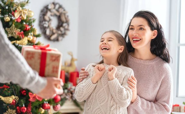 Merry Christmas and Happy Holidays! Mum, dad and child exchanging gifts. Parents and daughter having fun near tree indoors. Loving family with presents in room. - Fotoğraf, Görsel