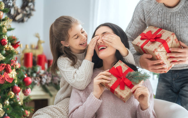 Merry Christmas and Happy Holidays! Mum, dad and child exchanging gifts. Parents and daughter having fun near tree indoors. Loving family with presents in room. - Foto, imagen