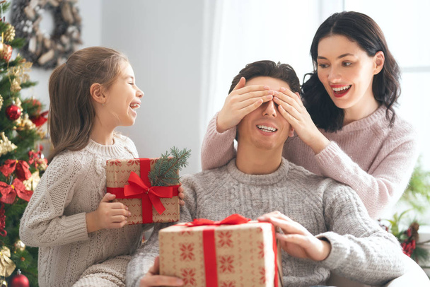 Merry Christmas and Happy Holidays! Mum, dad and child exchanging gifts. Parents and daughter having fun near tree indoors. Loving family with presents in room. - Foto, Imagen