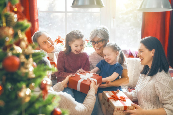 Merry Christmas and Happy Holidays! Grandma, grandpa, mum, dad and child exchanging gifts. Parents and daughter having fun near tree indoors. Loving family with presents in room. - Photo, image