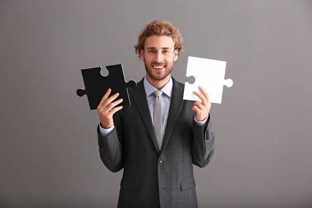 Young businessman with pieces of jigsaw puzzle on grey background - Zdjęcie, obraz