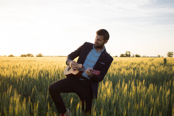 Happy manager with ukulele travel in summer wheat fields, buisinesman in suit play on ukulele, vacation or travel concept photo - Foto, Imagen