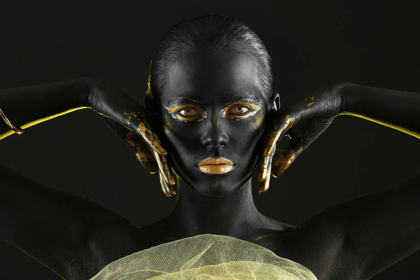 Beautiful woman with black and golden paint on her body against dark background - Photo, Image