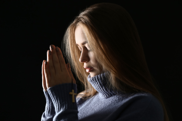 Όμορφη νεαρή γυναίκα που προσεύχεται σε σκούρο φόντο - Φωτογραφία, εικόνα