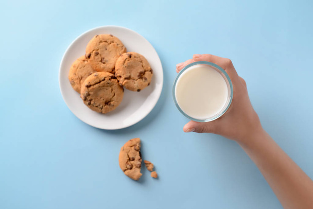 Female hand with glass of milk and tasty cookies on color background - Photo, Image