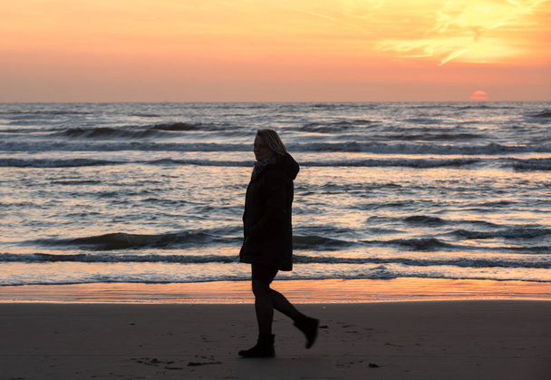 Katwijk, Netherlands - April 23, 2017: Woman walking on beach in Katwijk at sunset. Netherlands - Photo, Image