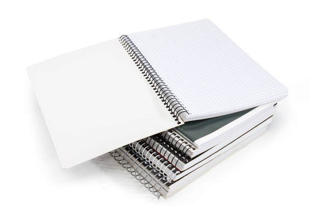 Libro de ejercicios en blanco abierto con páginas de papel cuadrado y encuadernación en espiral de alambre en la pila de otros libros de ejercicios sobre un fondo blanco
 - Foto, Imagen