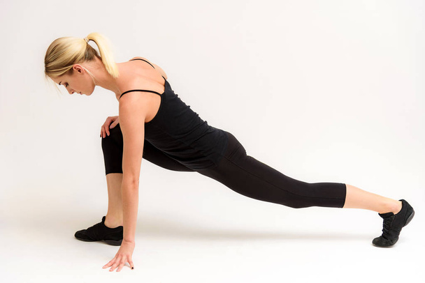 Studio photo of a beautiful blonde girl doing fitness stretching exercises on a white background. She is right in front of the camera, smiling and looking happy. - Foto, immagini