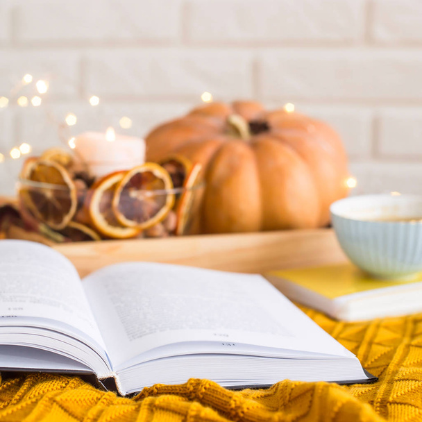 Descanso acogedor acogedor en un día de otoño - leyendo entre mantas con una taza de café al lado de velas, naranjas secas y calabaza
 - Foto, imagen