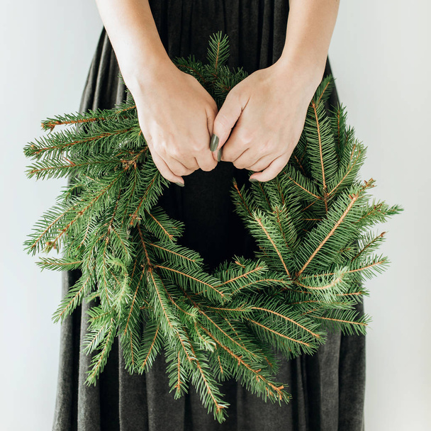 Молодая женщина держит венок, сделанный из еловых ветвей. Рождественская / Новогодняя композиция
. - Фото, изображение