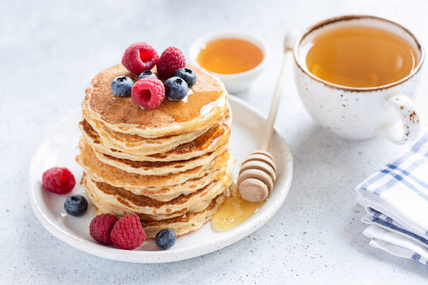 Stack of healthy oat pancakes with berries, honey and cup of green tea - Fotó, kép