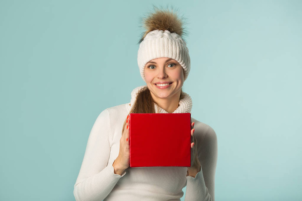 szép, fiatal lány a kalapban egy ajándékkal a kezében, kék háttérrel - Fotó, kép