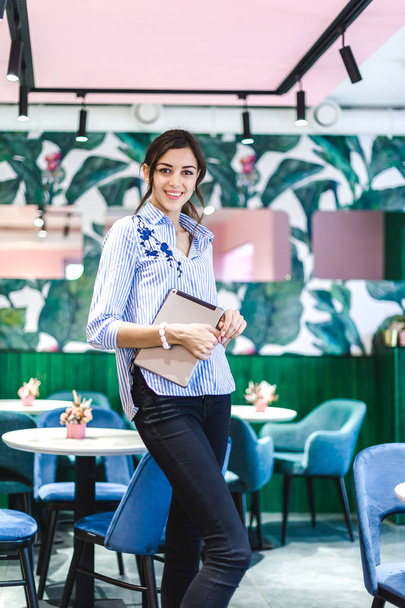 Workplace women in a cafe. portrait of a young fresh brunette with a tablet in hand in the interiors with pink color - Foto, Bild