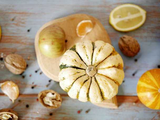 Гарбуз яскраво-жовтий зі смугами на обробній дошці, на дерев'яному столі на тлі сезонних овочів, фруктів, горіхів, приготування здорової їжі
 - Фото, зображення