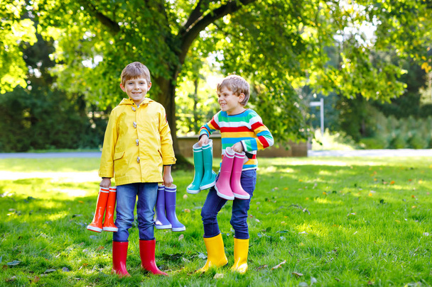Two little kids boys, cute siblings with lots of colorful rain boots. Children in different rubber boots and jackets. Footwear for rainy fall. Healthy twins and best friends having fun outdoors - Photo, Image